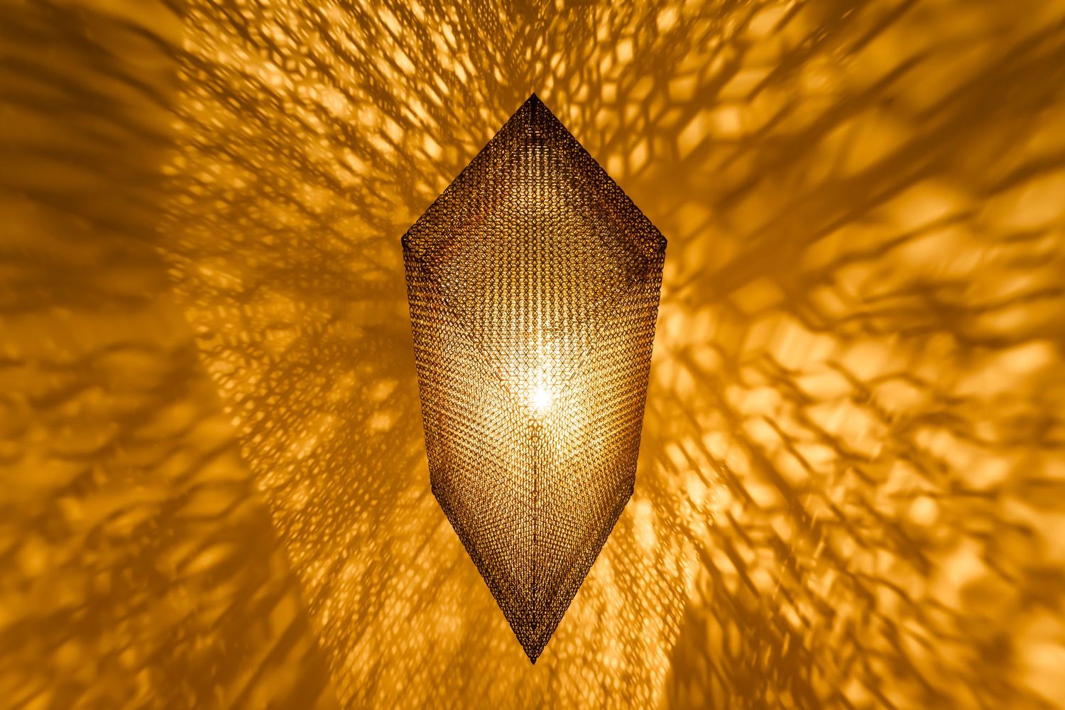 Diamond-shaped latticed lamp casting dramatic golden light patterns on wall.