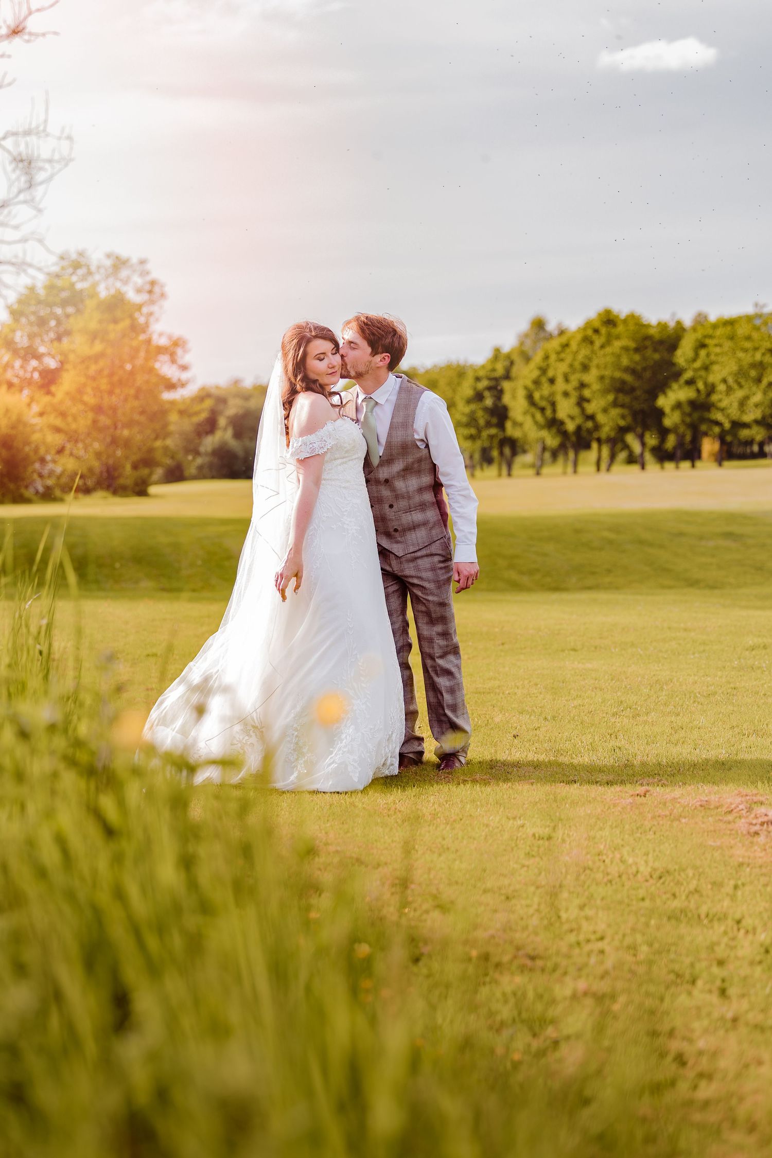Wedding couple embracing in a lush meadow during sunset with long grass in the foreground.