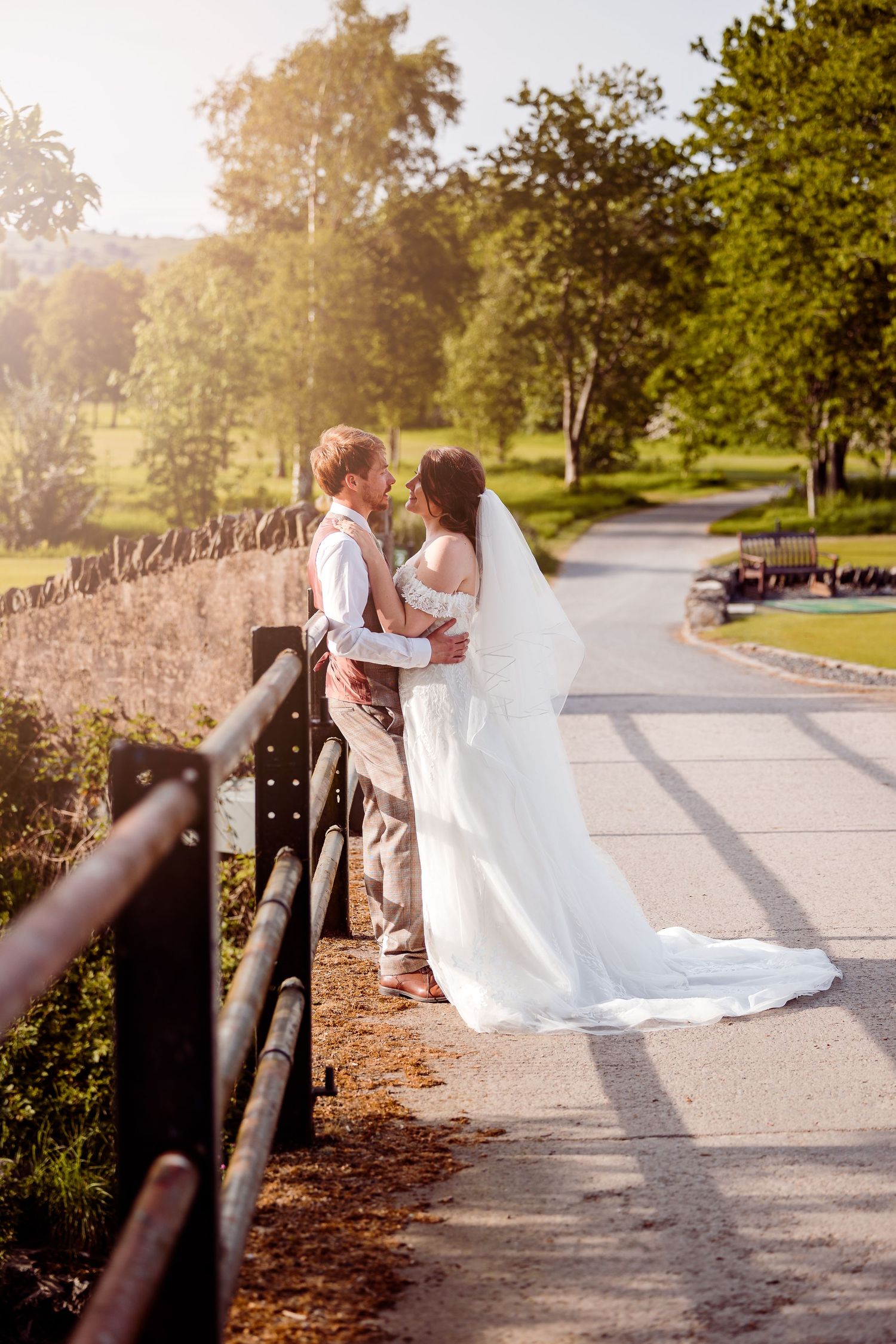 Couple in wedding attire standing by a rustic fence during golden hour.