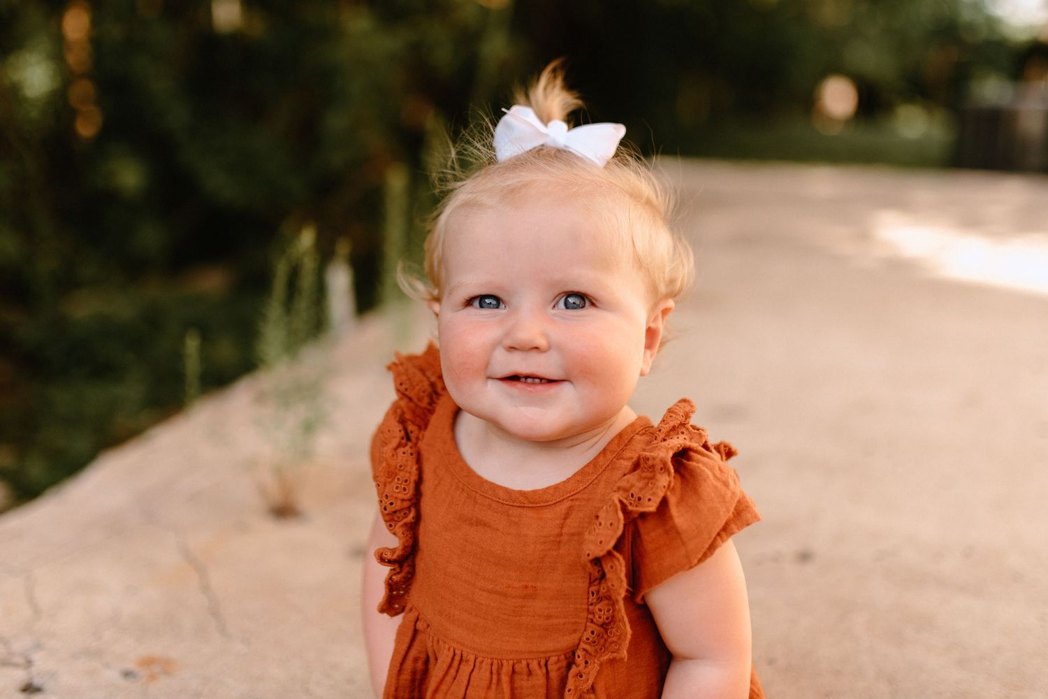 Young child in orange ruffled dress smiling at camera in outdoor setting.