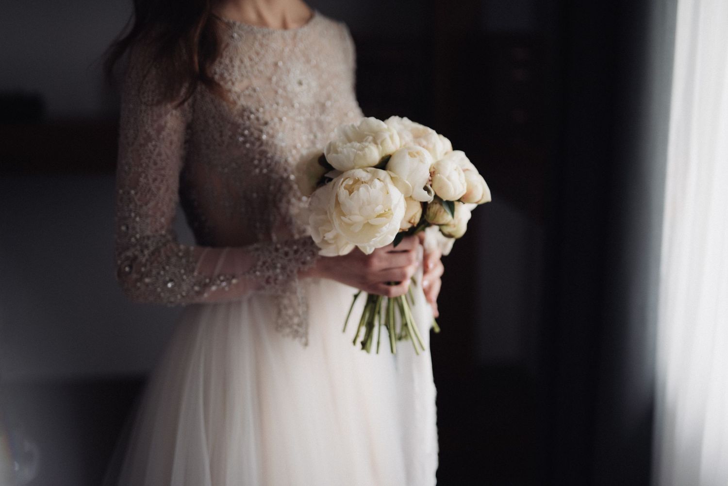 Close-up of bride holding classic white peony bouquet in lace-detailed wedding dress.