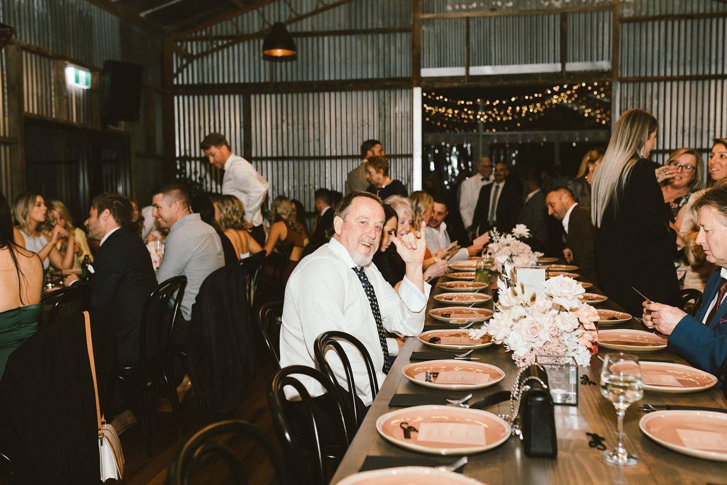 Reception venue decorated with string lights and round tables with pink place settings.