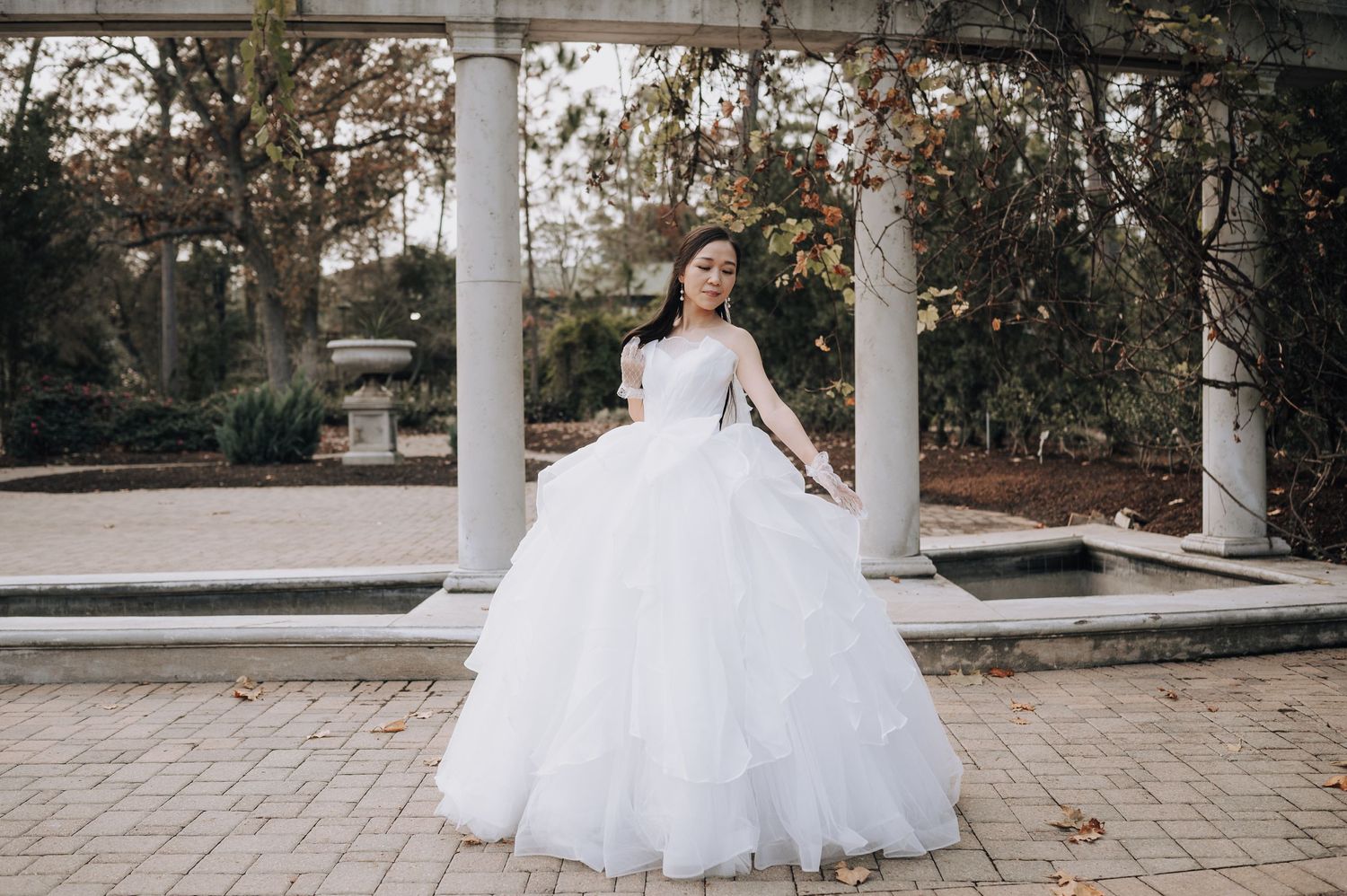 Bride in voluminous white ball gown posing elegantly between classic white columns.