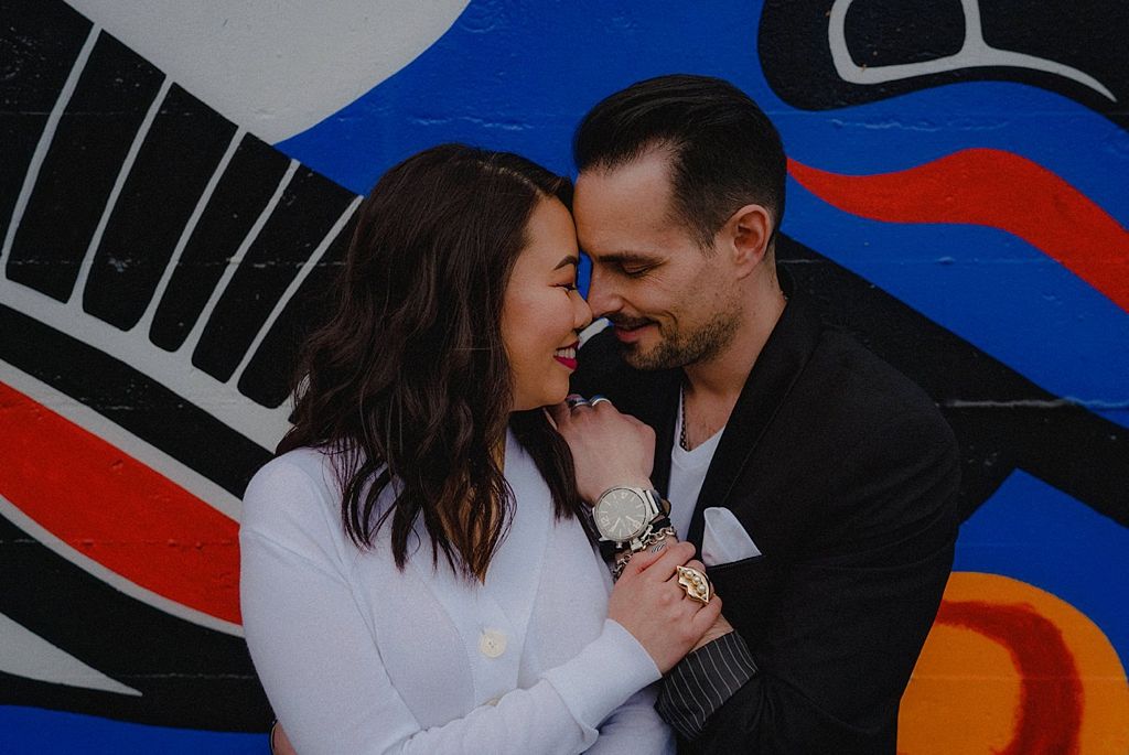 A couple shares an intimate moment against a bold graphic mural with red and blue patterns.