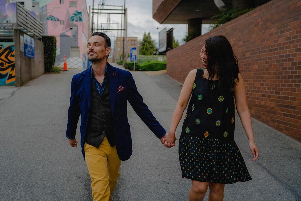 Couple walking hand in hand on urban sidewalk with man wearing bright yellow pants.