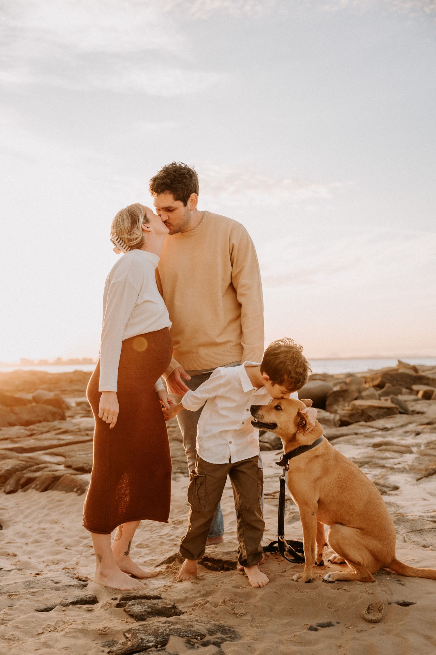 A tender family moment on rocky coastal terrain at sunset with their faithful golden retriever.
