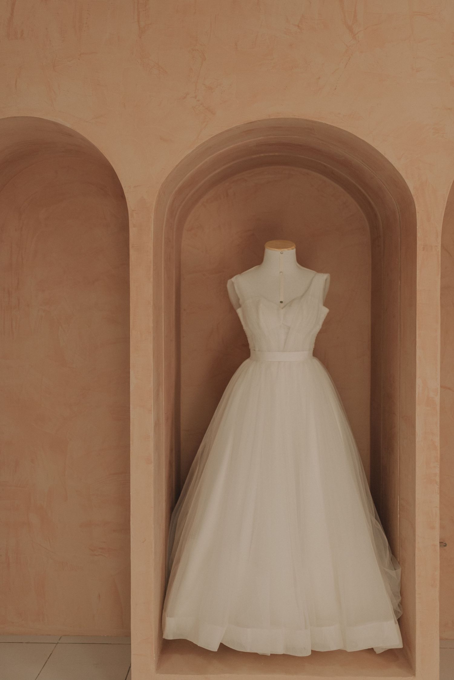 A white wedding dress on display in an arched terracotta wall niche.