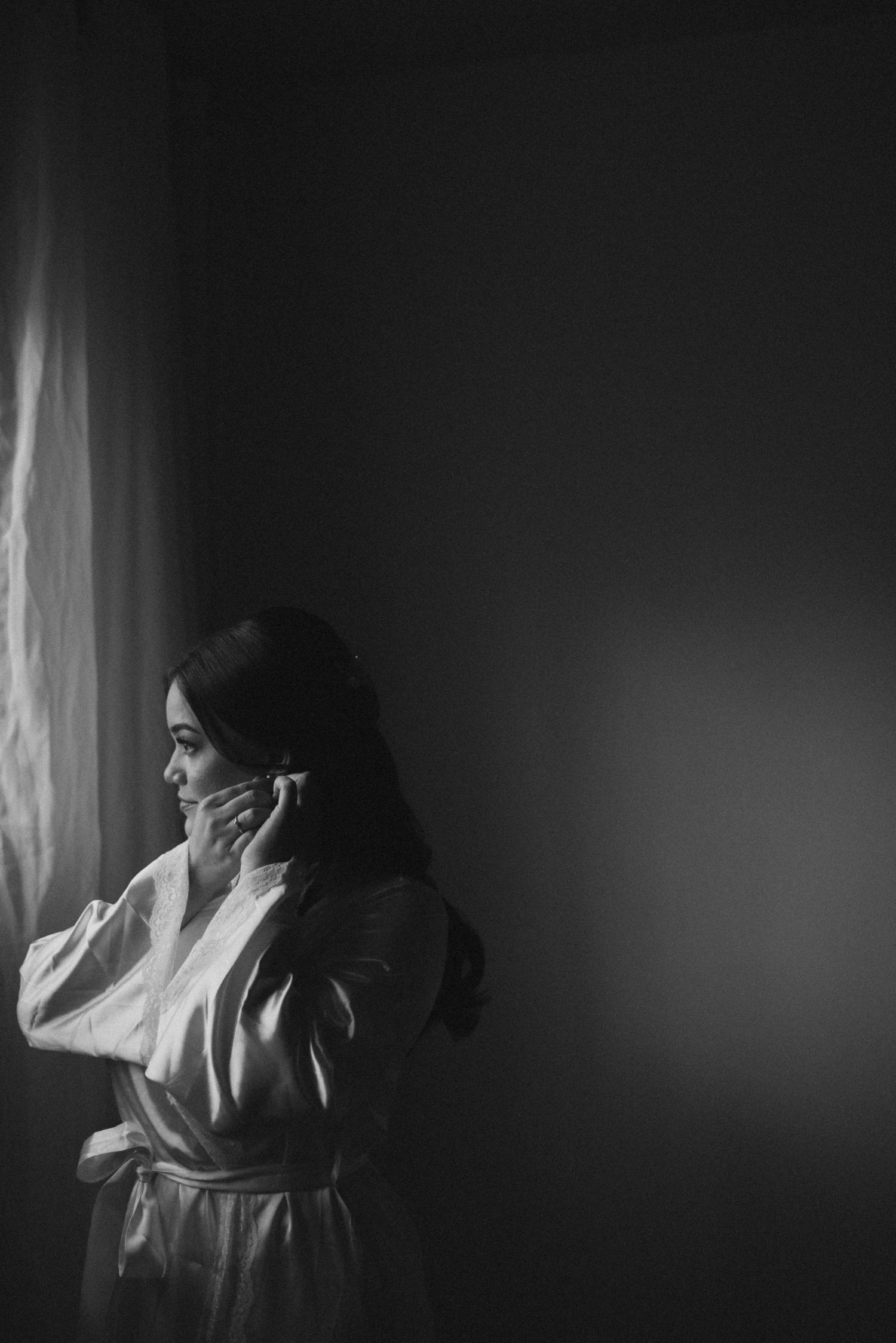 Moody black and white photo of person in white robe by window.