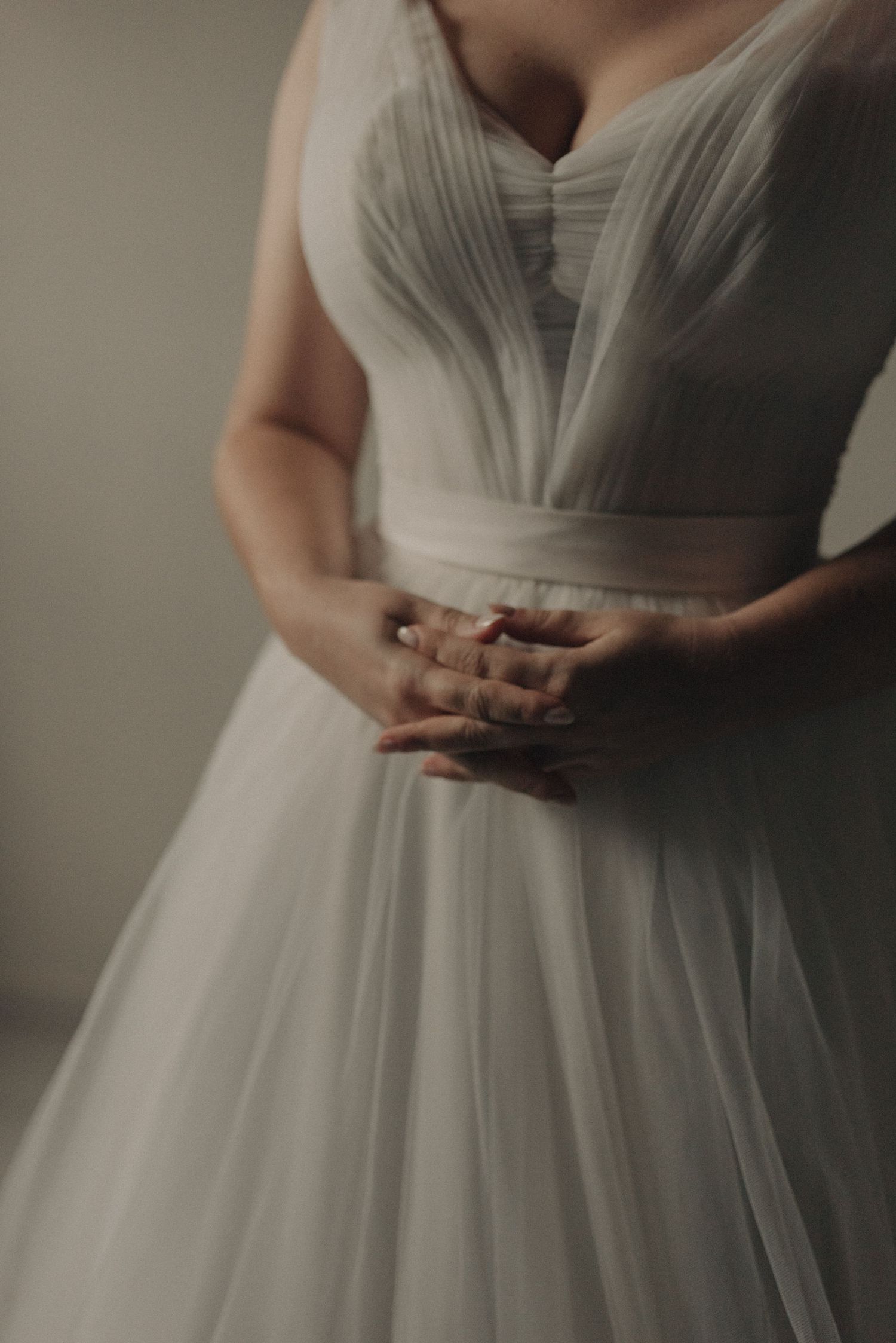 Detail shot of hands resting on pleated white wedding dress bodice.