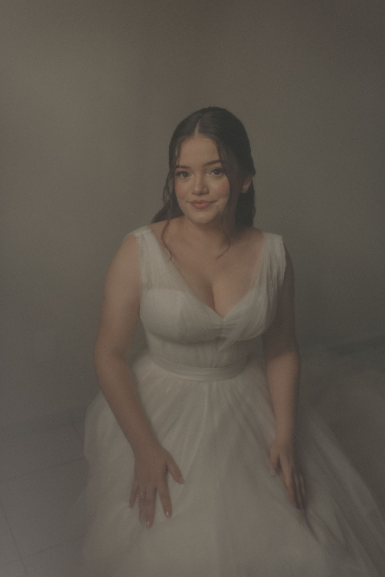 A bride poses in a classic white wedding gown with a sweetheart neckline in a moody studio portrait.