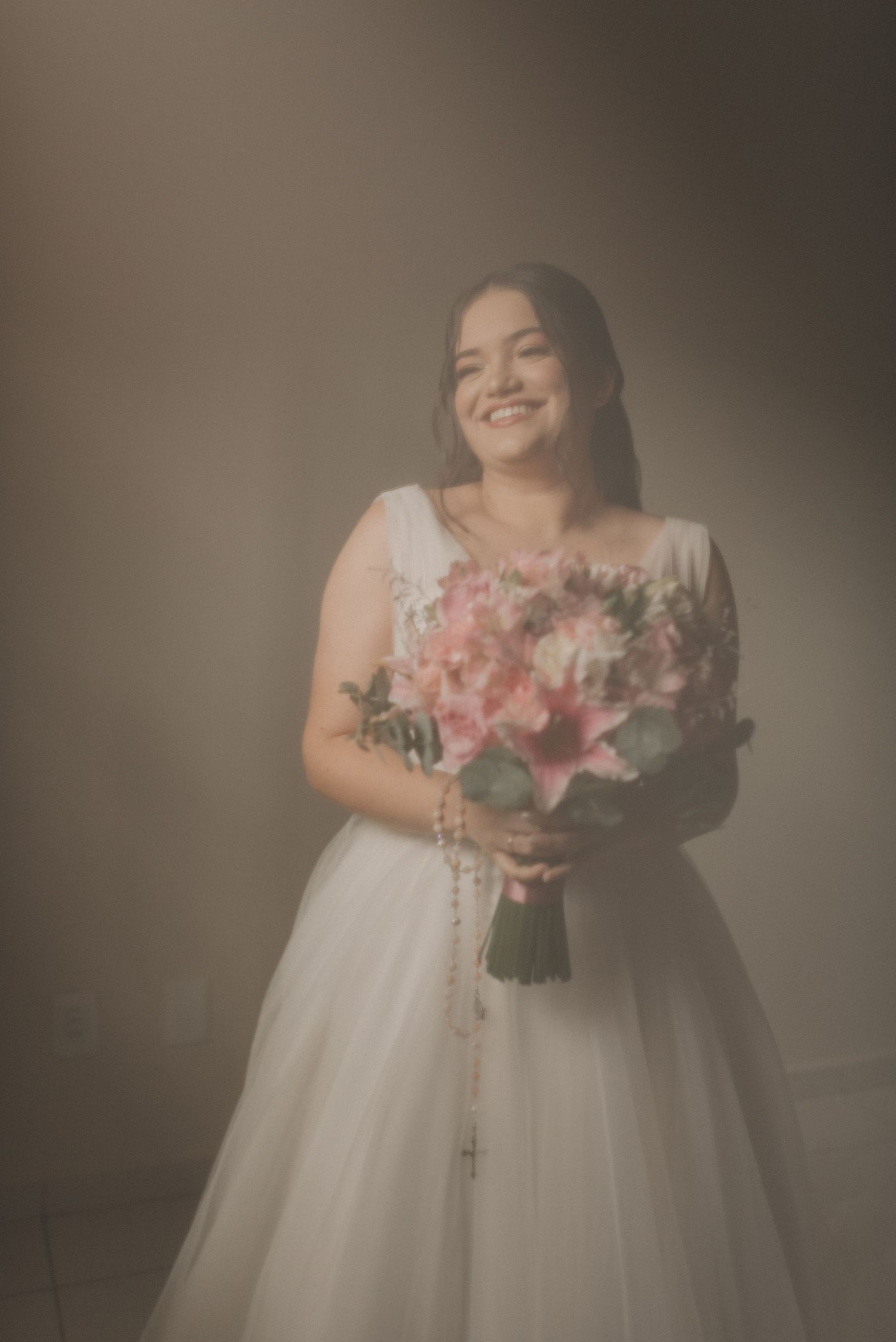 A joyful bridal portrait with a pink and white floral bouquet against a neutral background.