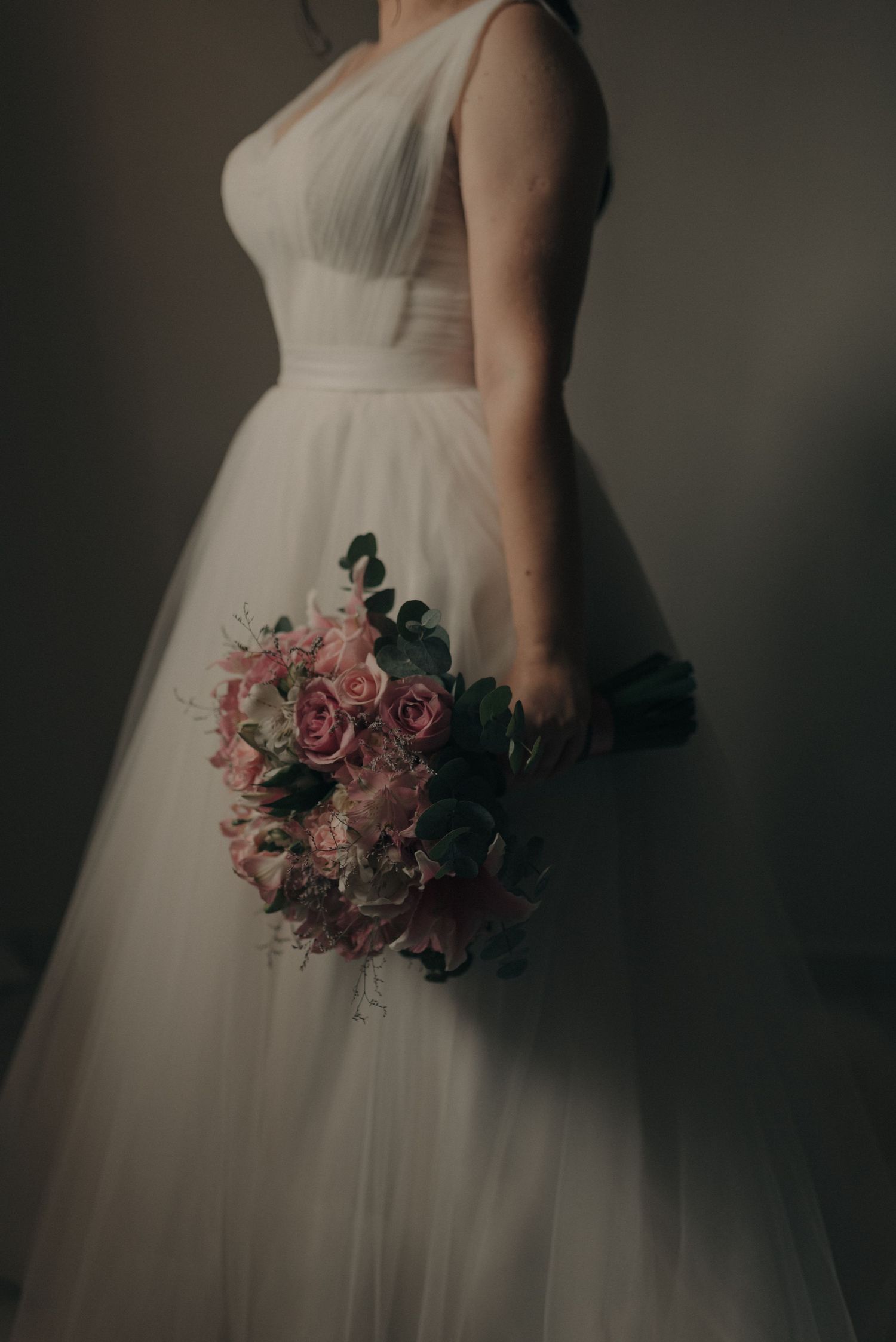 Side view of a bride in a white tulle gown holding a pink and green floral bouquet.