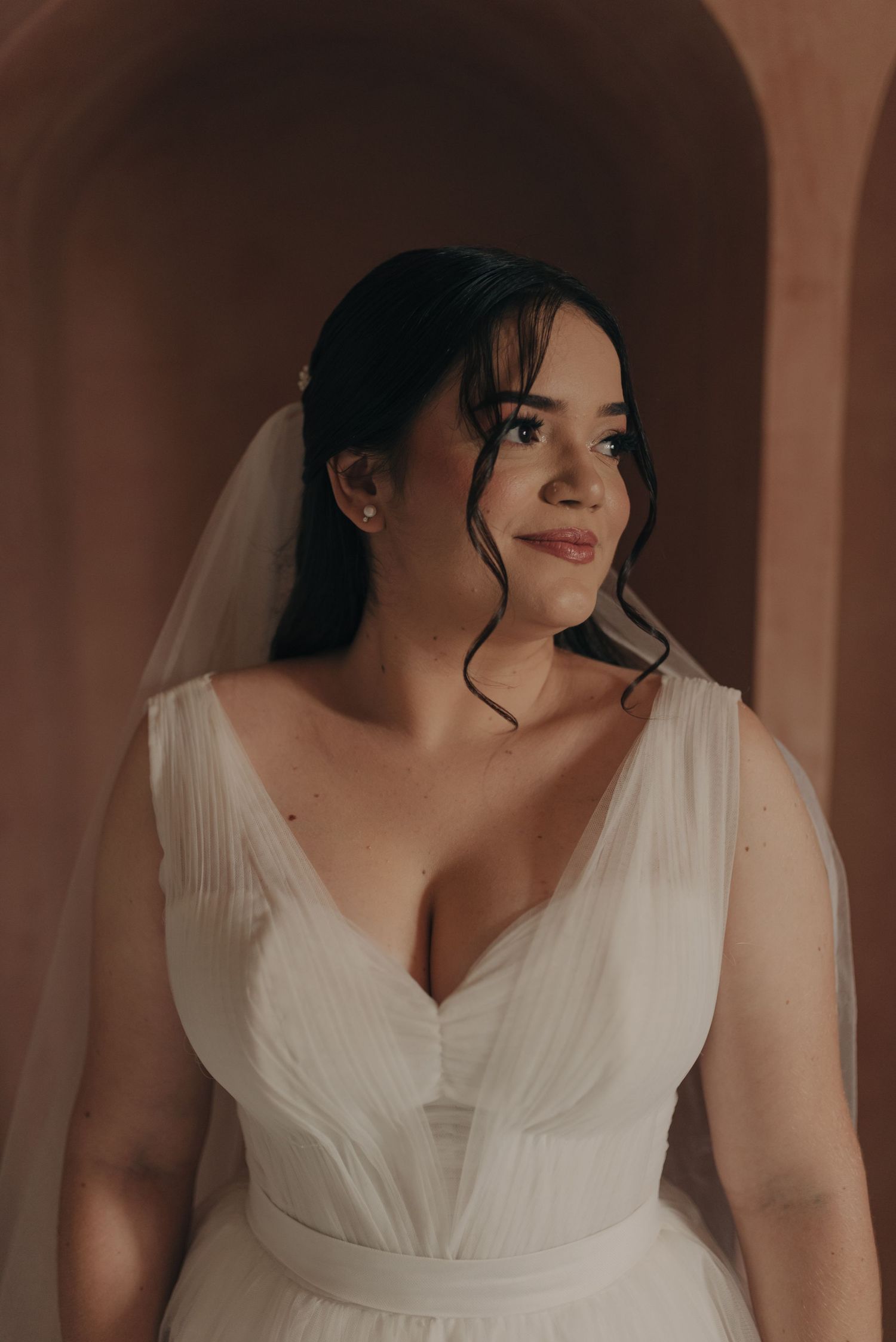 A bride in a white V-neck wedding gown poses in front of an arched terracotta wall.