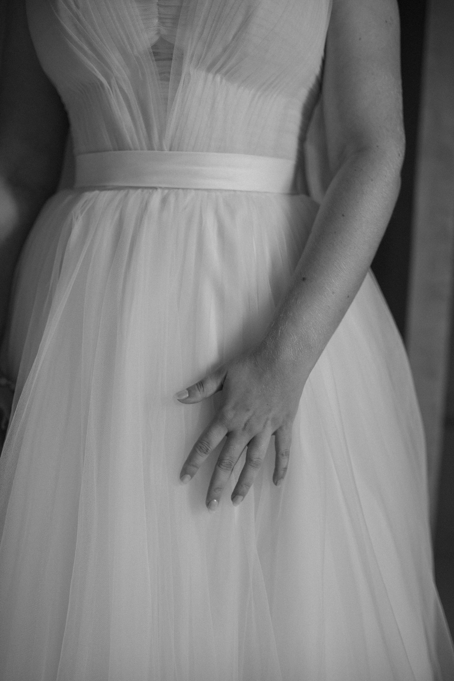 Close-up black and white detail of a bride's hand against her flowing tulle wedding dress.