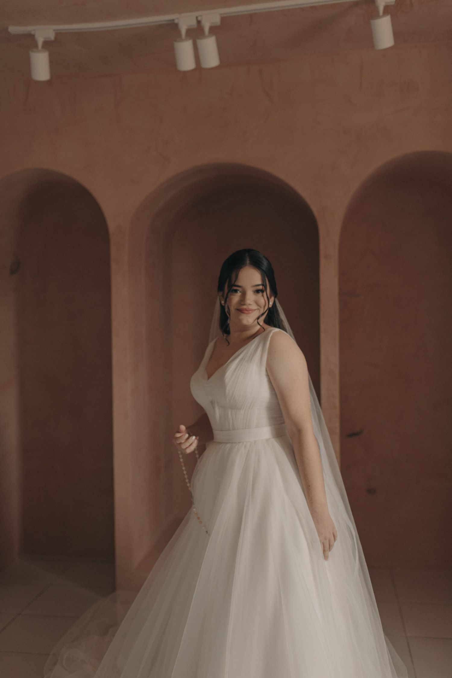 Full-length bridal portrait in a romantic setting with arched terracotta walls.