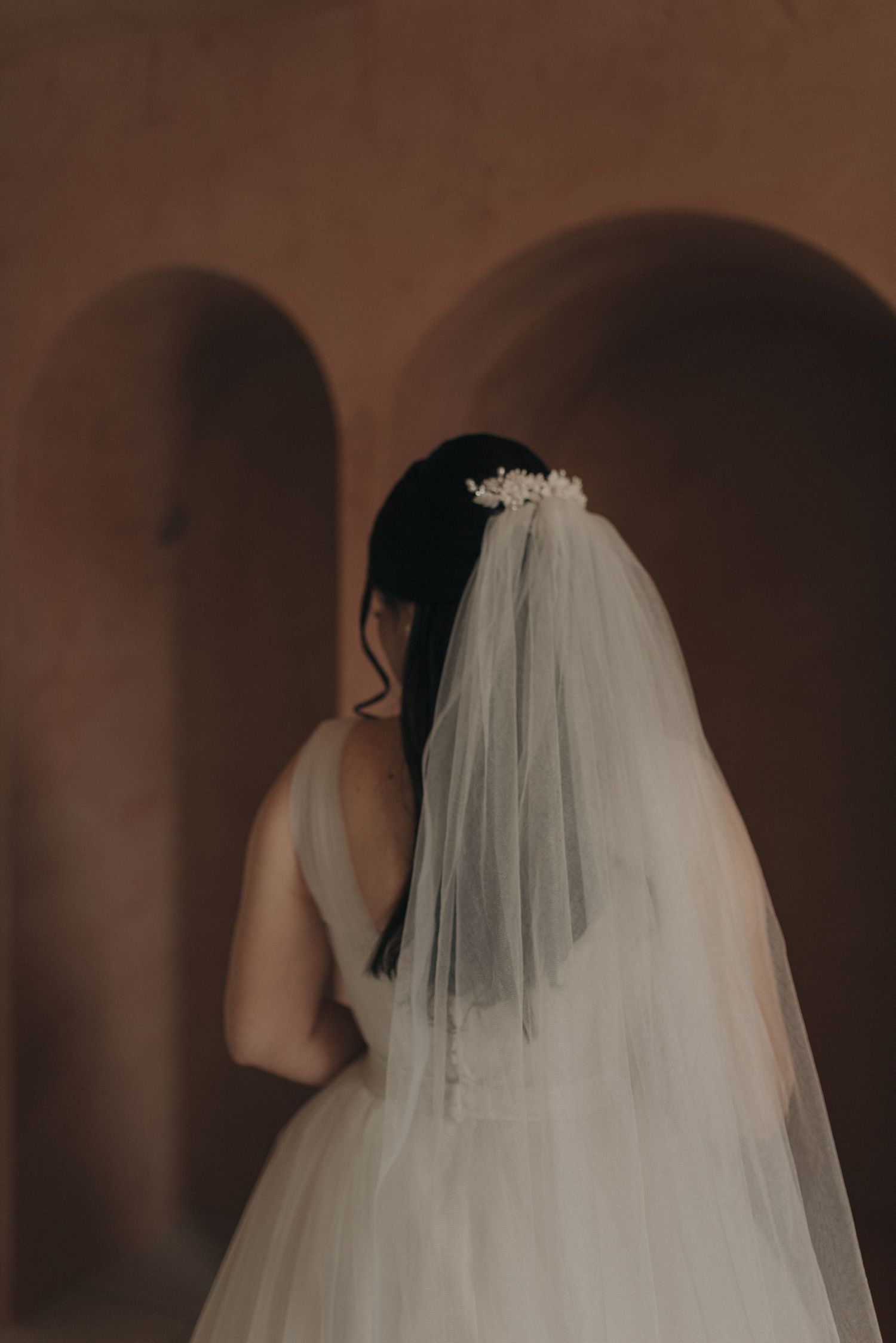 Back view of a bride's veil and dark hair against warm terracotta walls.