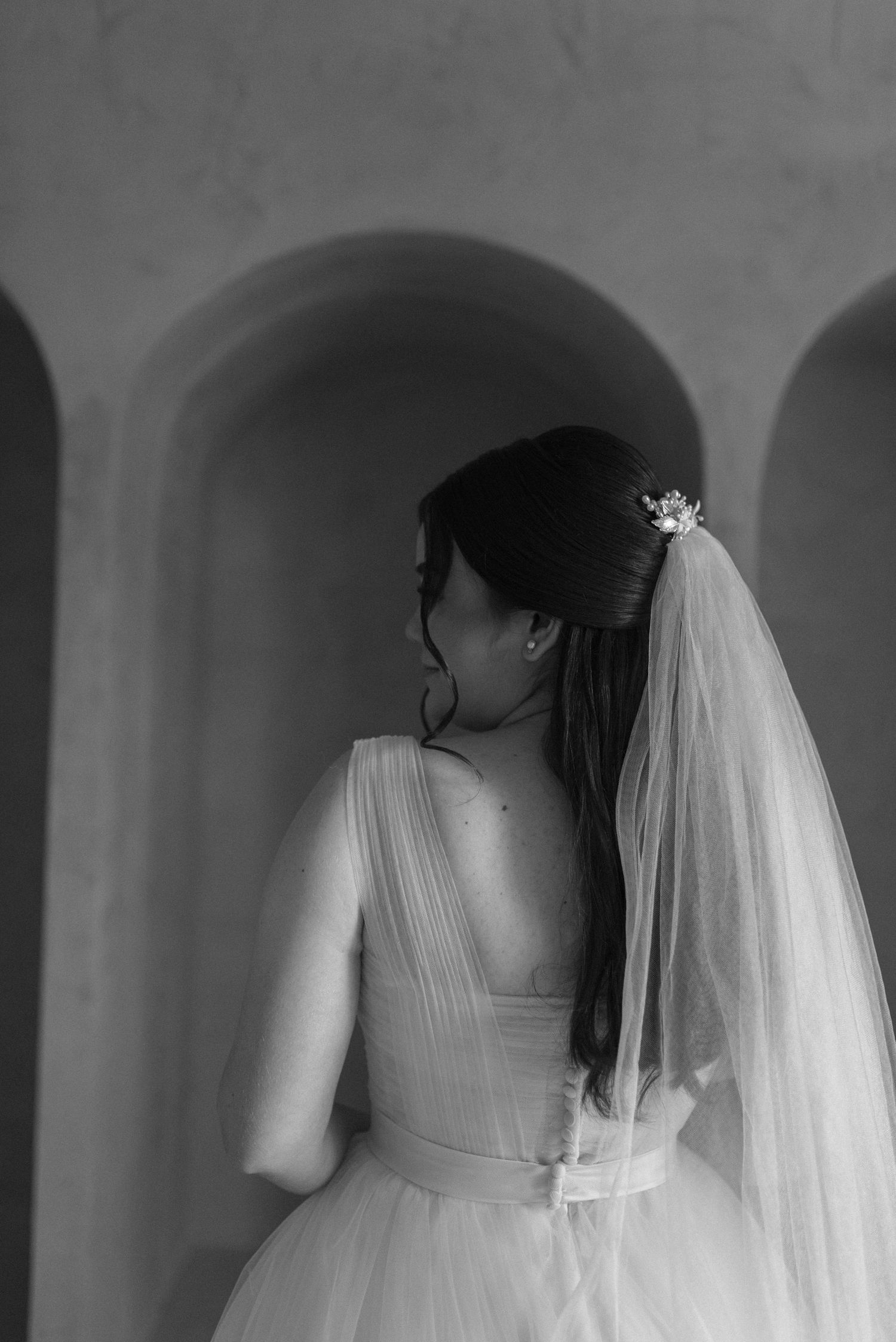 Black and white portrait showing the back detail of a bride's dress and veil.