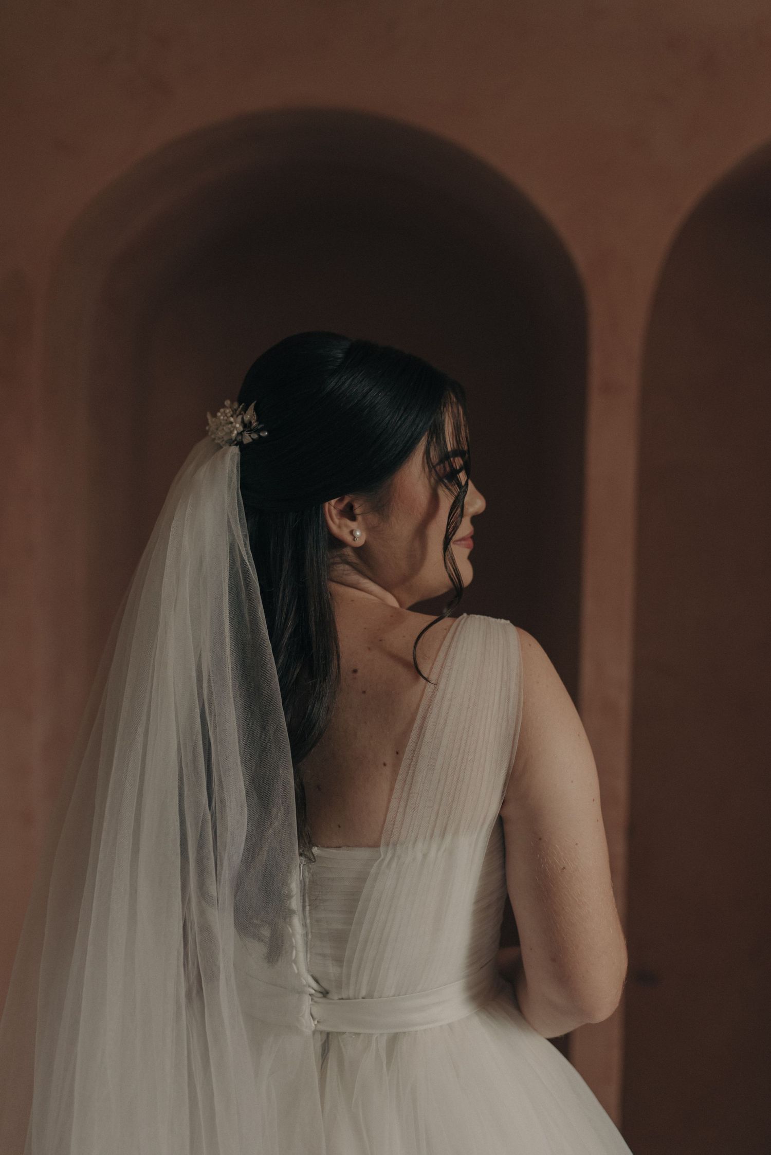 Side portrait of a bride in a classic wedding dress against warm terracotta walls.