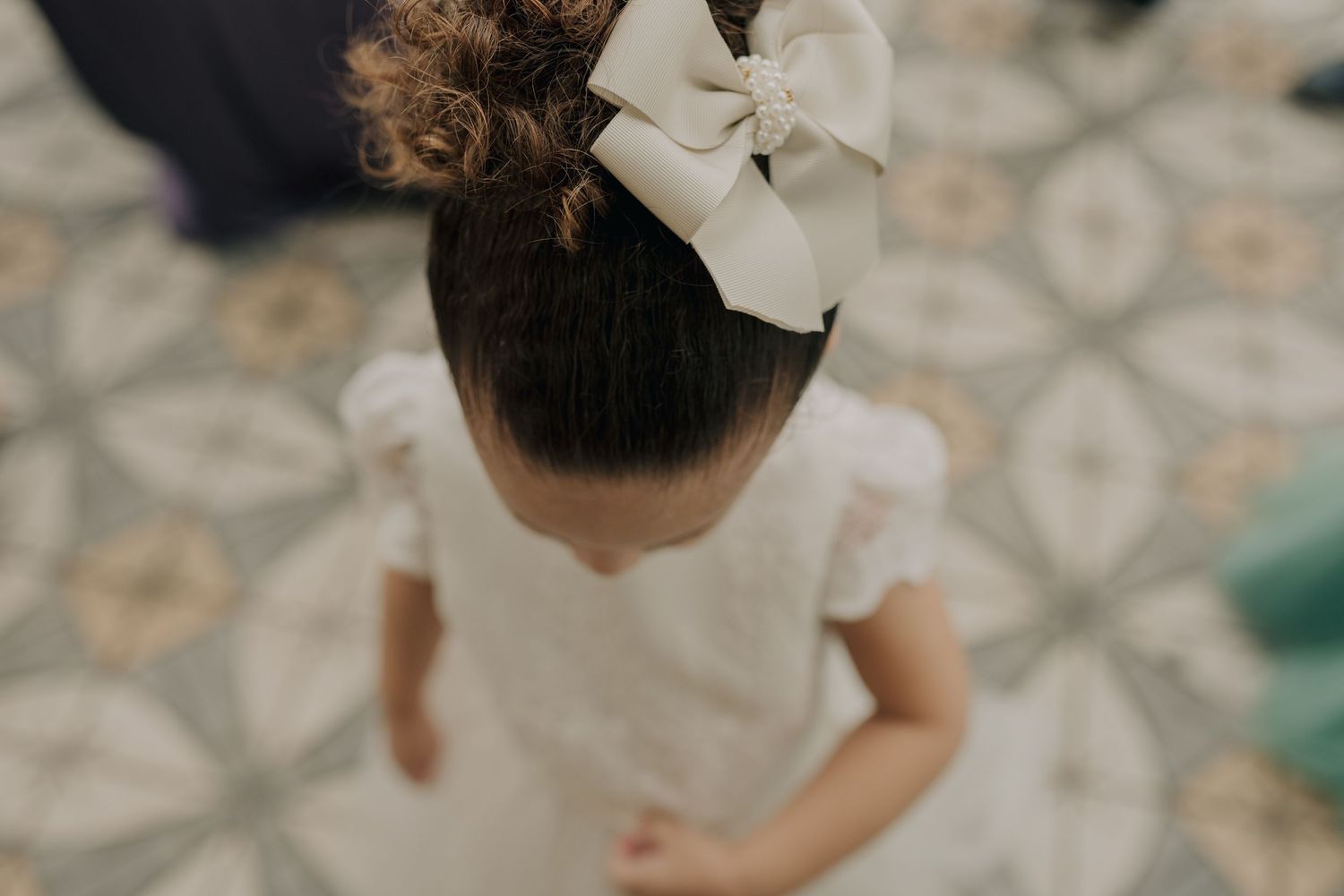 Overhead view of a white bow adorning an elegant updo hairstyle against patterned floor tiles.