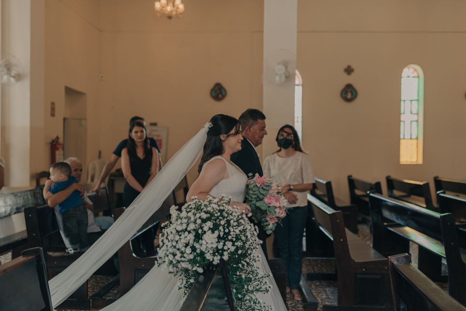 Wedding party gathered inside church with wooden pews and stained glass windows visible.
