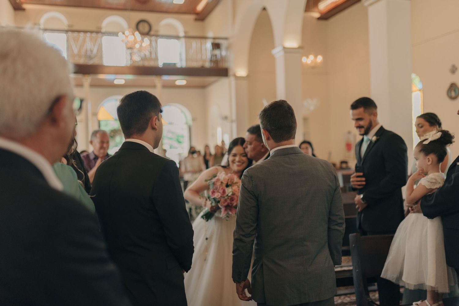 Wedding attendees standing in a beautiful church sanctuary with arched windows and wooden beams.