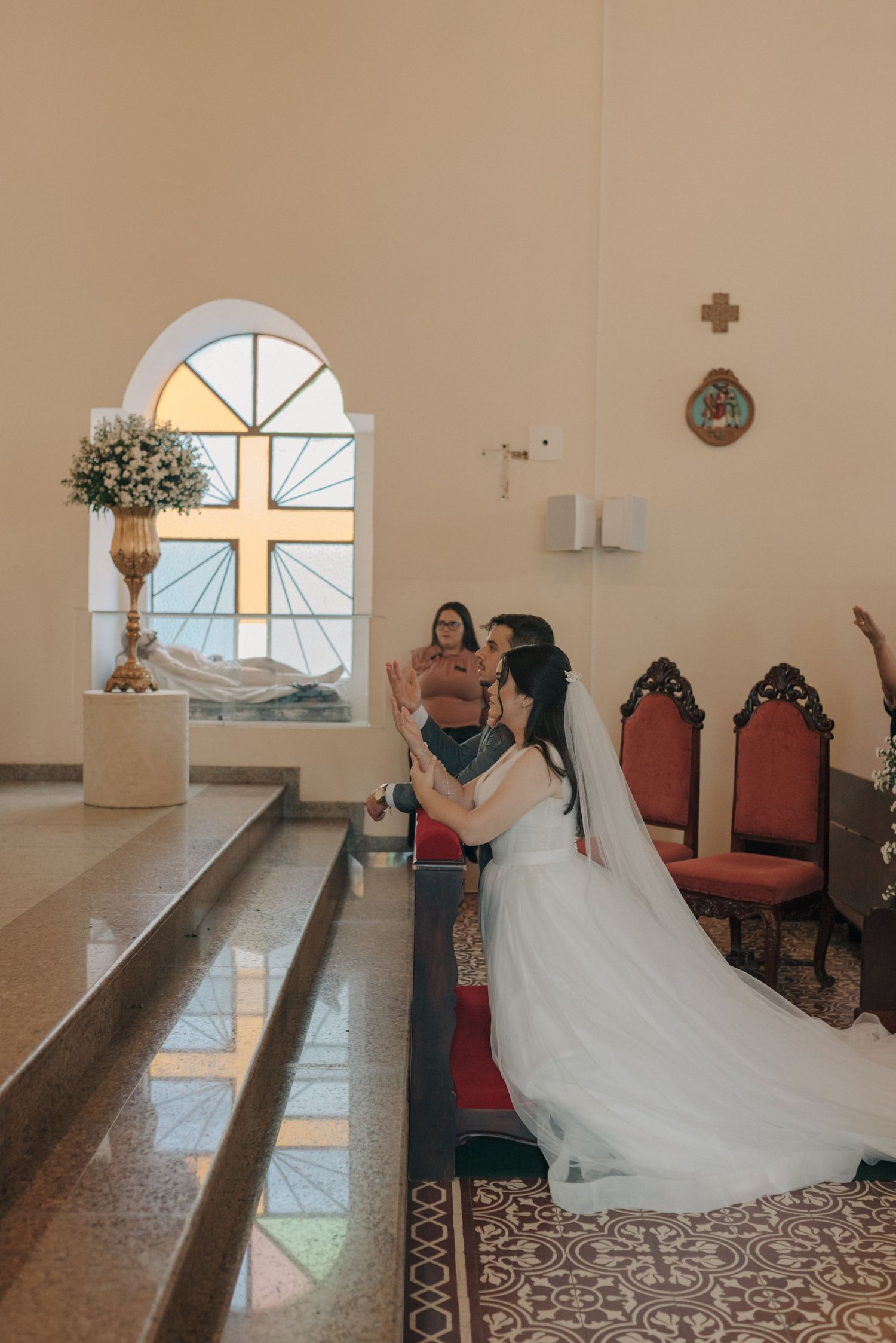 Church interior with stained glass window and wedding dress train flowing on tiled floor.