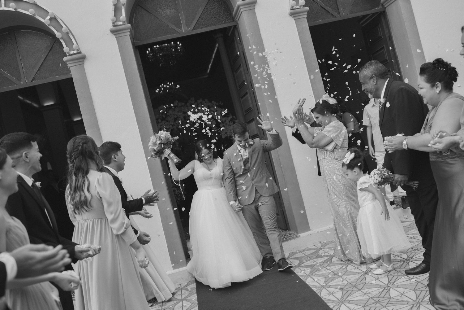 Black and white photo of wedding exit with guests throwing confetti outside church arches.
