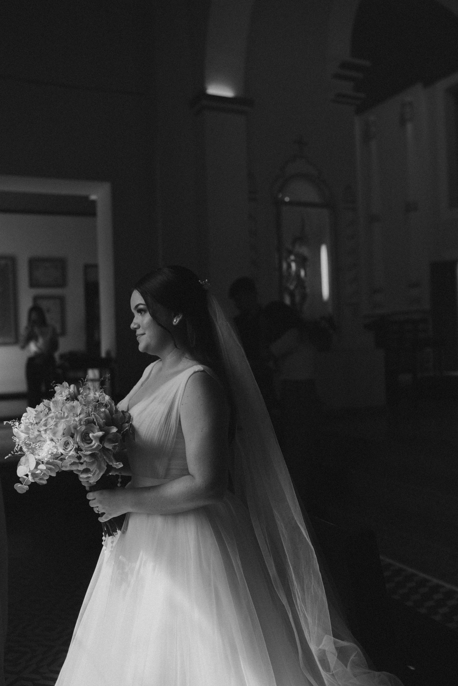 A black and white portrait of a bride holding her bouquet in a church setting.