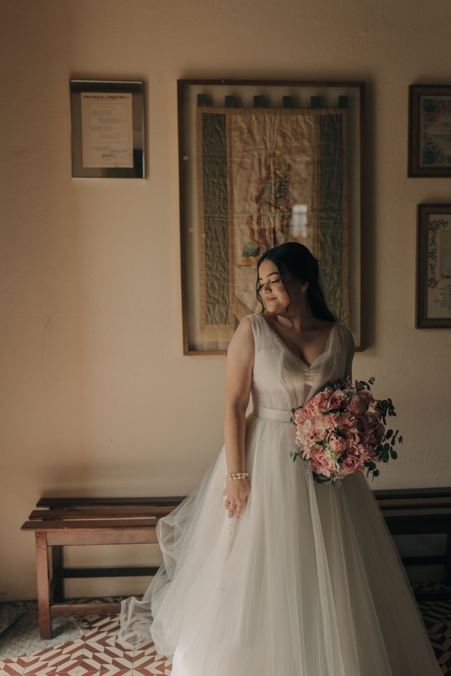A bride in a flowing white gown holds a pink bouquet against framed wall art.
