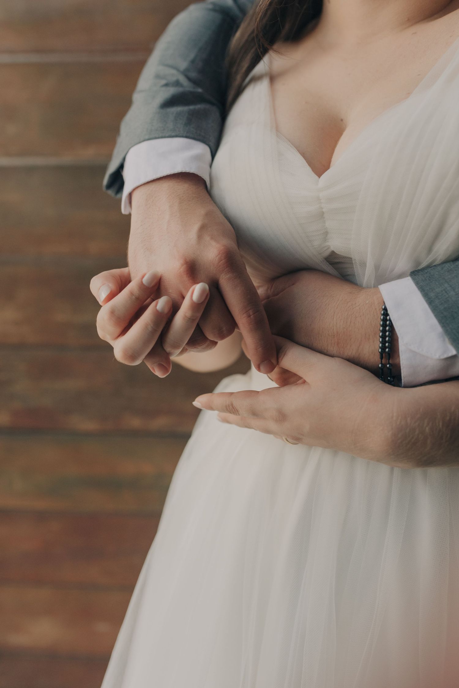 Close-up of couple's hands embracing, showing wedding dress and suit details.