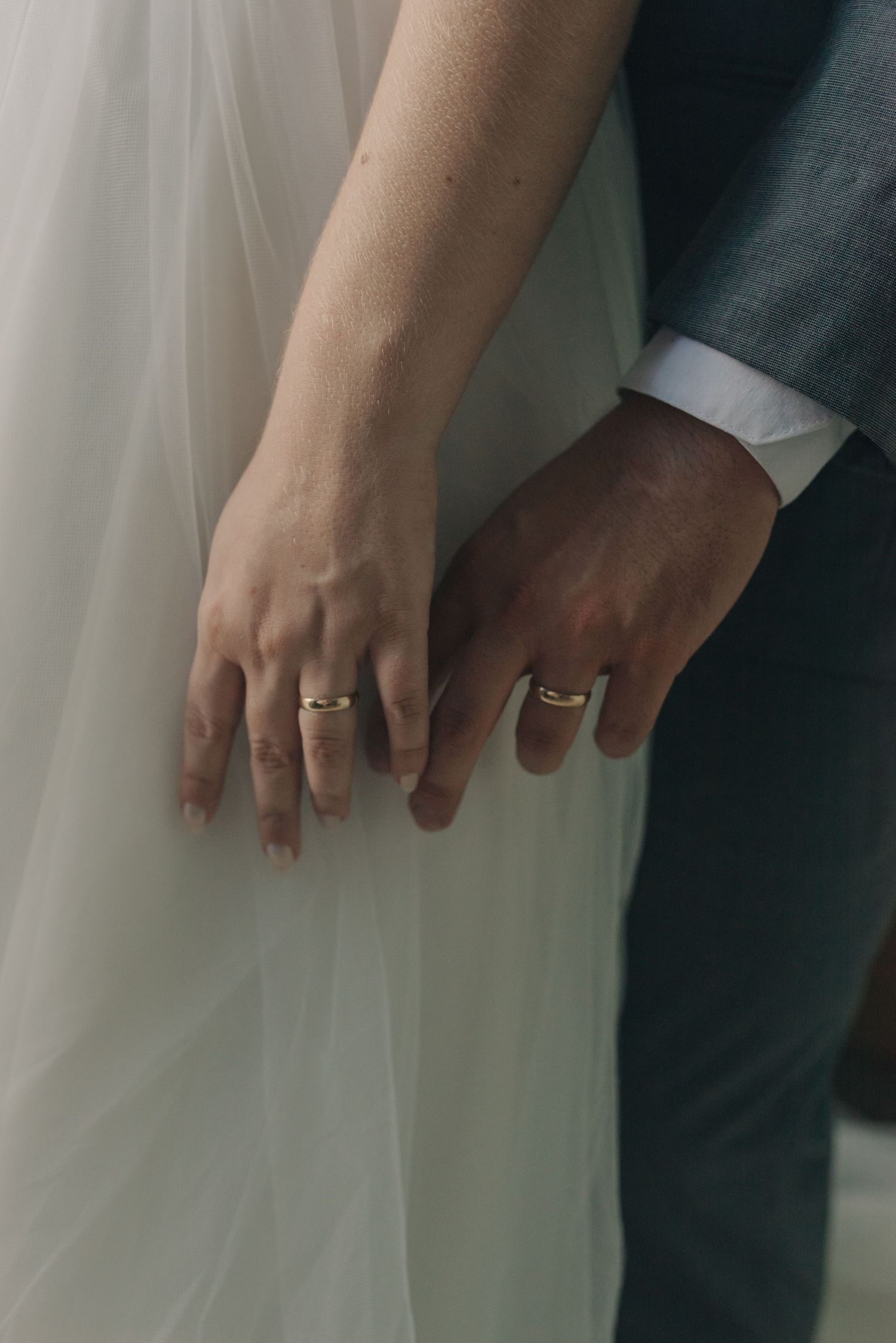 Detail shot of newlyweds' hands with wedding rings against dress and suit.