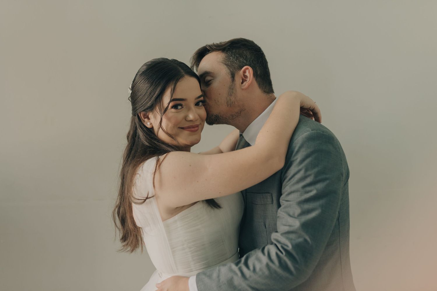 Intimate embrace of newlyweds in romantic portrait against neutral background.