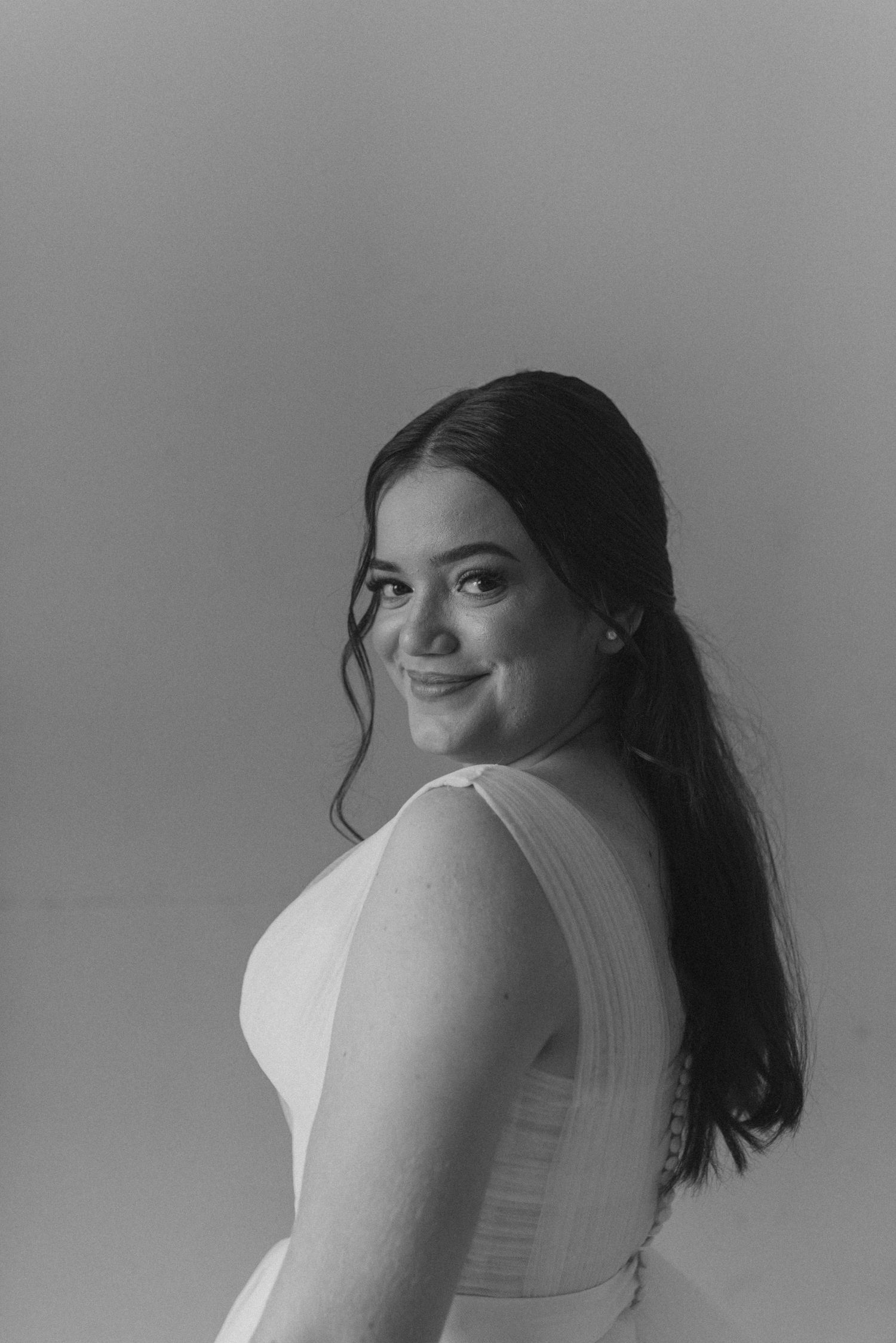 Portrait in black and white showing a joyful smile and long dark hair against a neutral background.