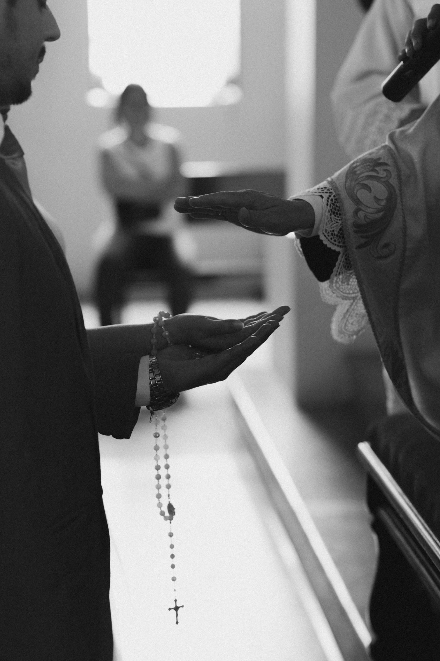 Black and white detail shot of hands holding a rosary during a Catholic wedding ceremony.