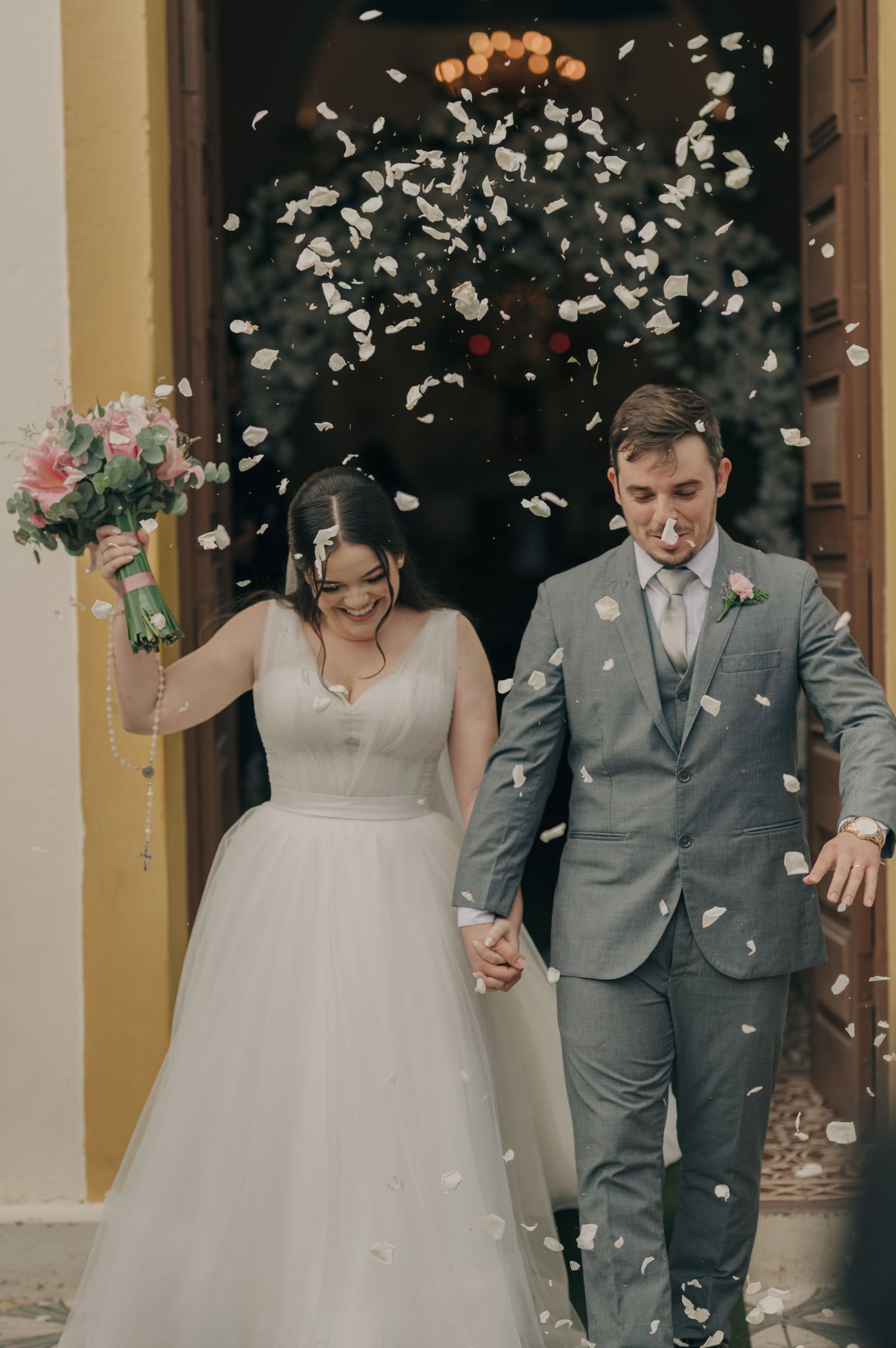 Newlyweds exit their wedding ceremony under a shower of white flower petals.