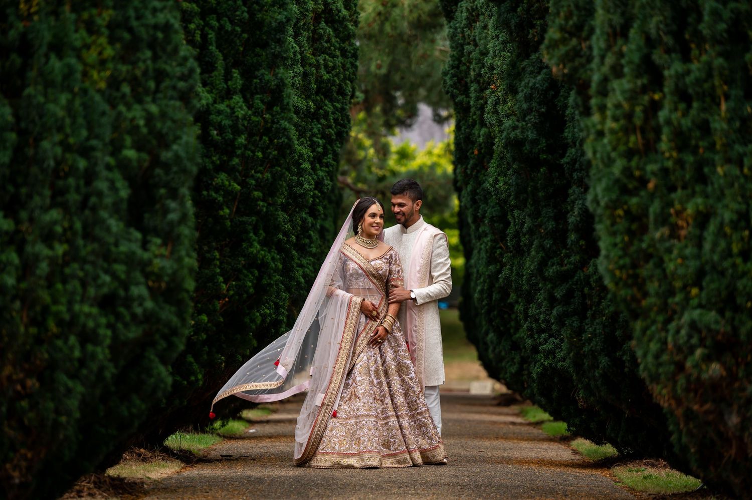 Romantic garden pathway lined with tall cypress trees creates perfect wedding photo backdrop.