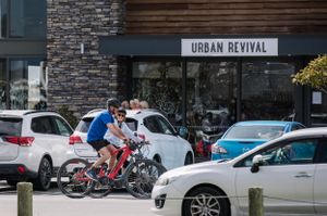 Cyclists riding past Urban Revival storefront with parked cars in front.