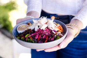 Colorful vegetarian bowl with purple cabbage, carrots and fresh toppings held in hands.