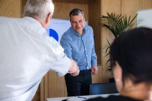Professional handshake between business partners in modern office with conference room.