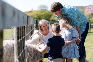 Family enjoying time together at a farm fence on a sunny day.