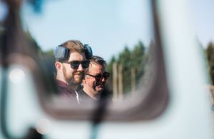 Reflection of two people wearing sunglasses captured in side mirror.