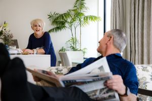 Couple relaxing at home with newspaper and houseplants in bright living room setting.