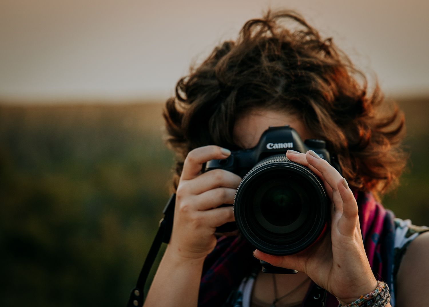 Someone photographs with a professional Canon camera against a sunset backdrop.