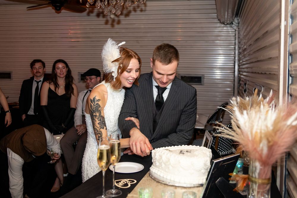 Wedding cake cutting moment in an elegant reception venue with chandelier overhead.