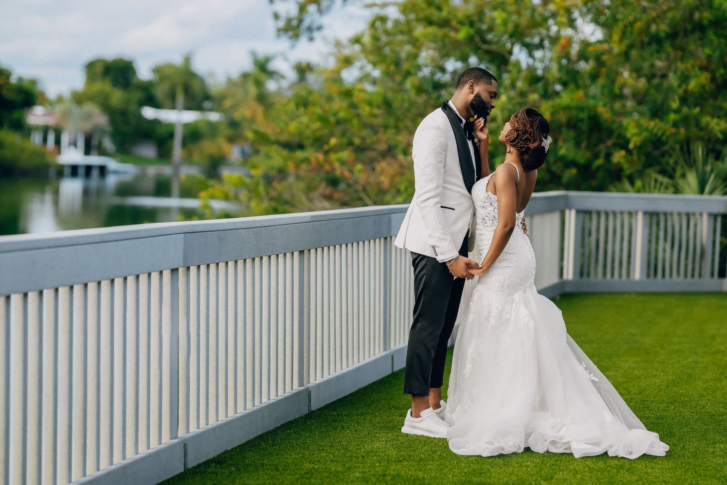 Bride and groom sharing romantic moment on waterfront bridge surrounded by lush greenery.
