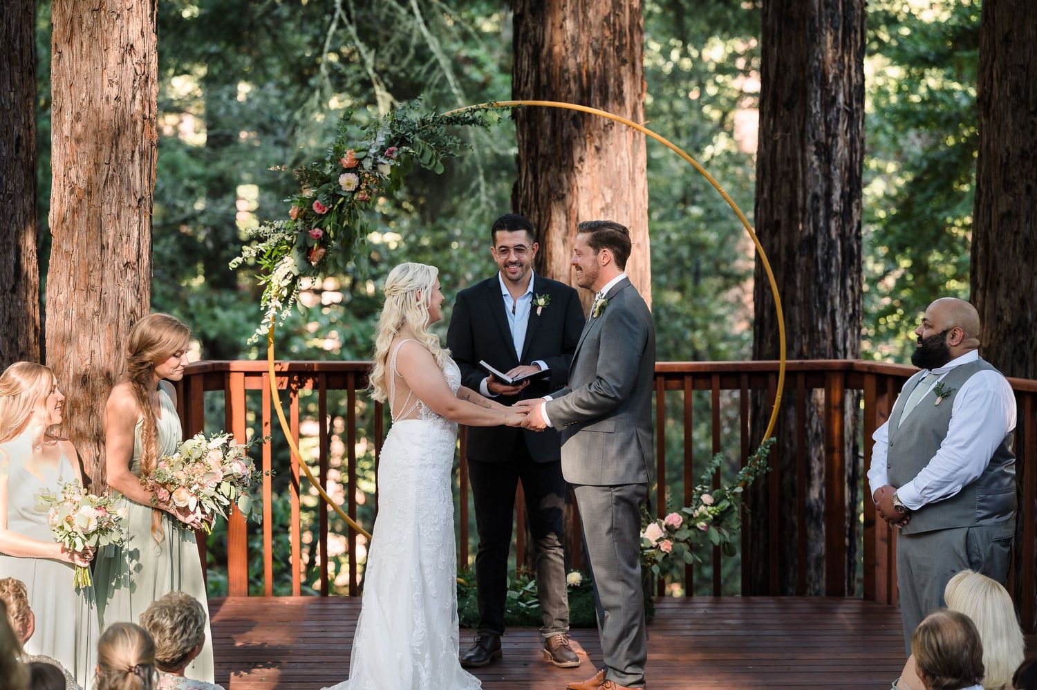 Outdoor wedding ceremony on a wooden deck surrounded by tall redwood trees.