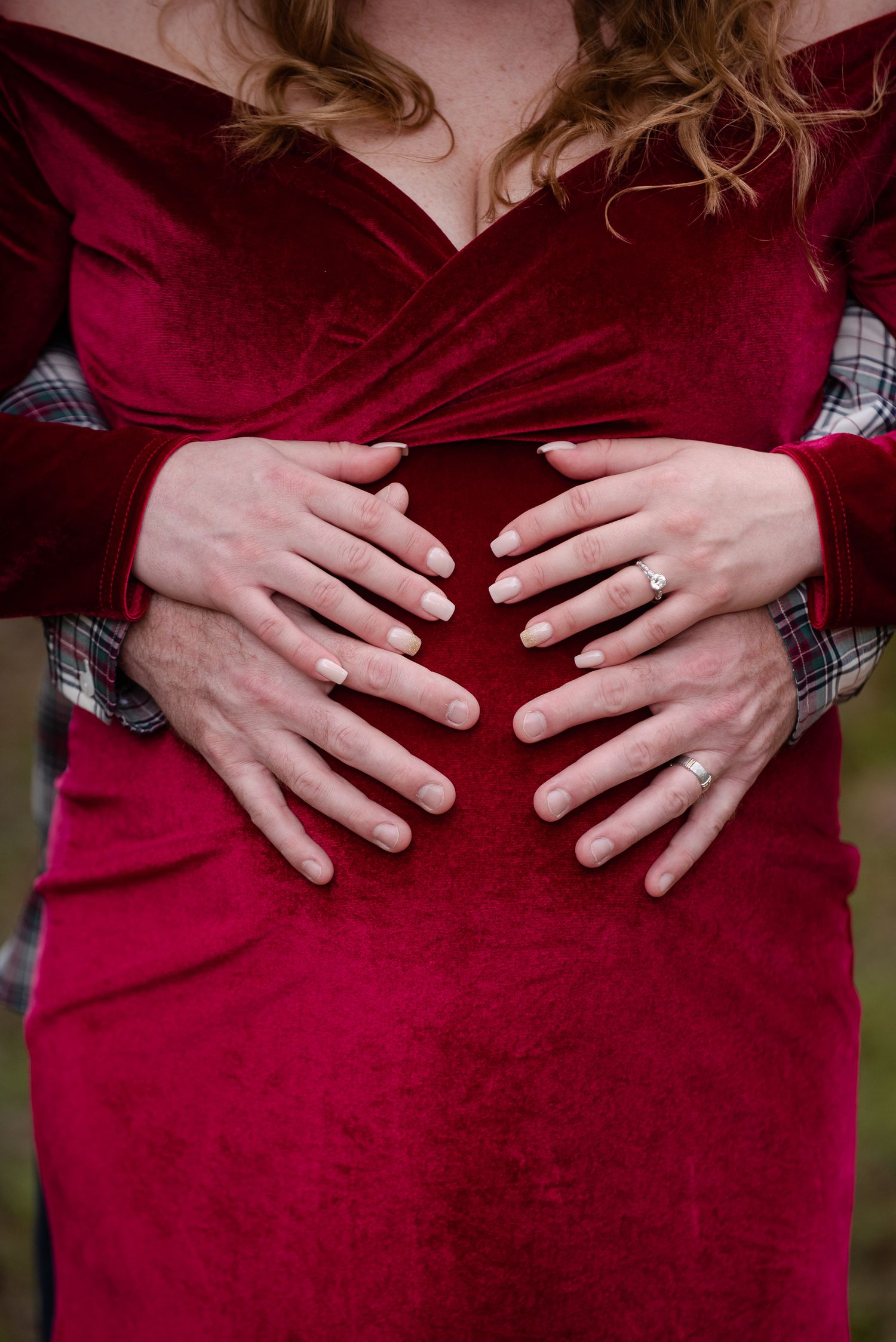 Hands forming a heart shape on a red velvet maternity dress.