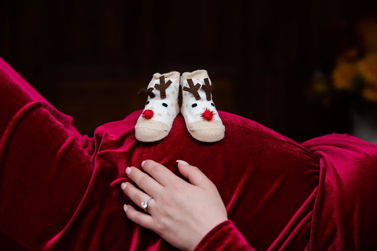 White baby shoes placed on a red velvet maternity dress.