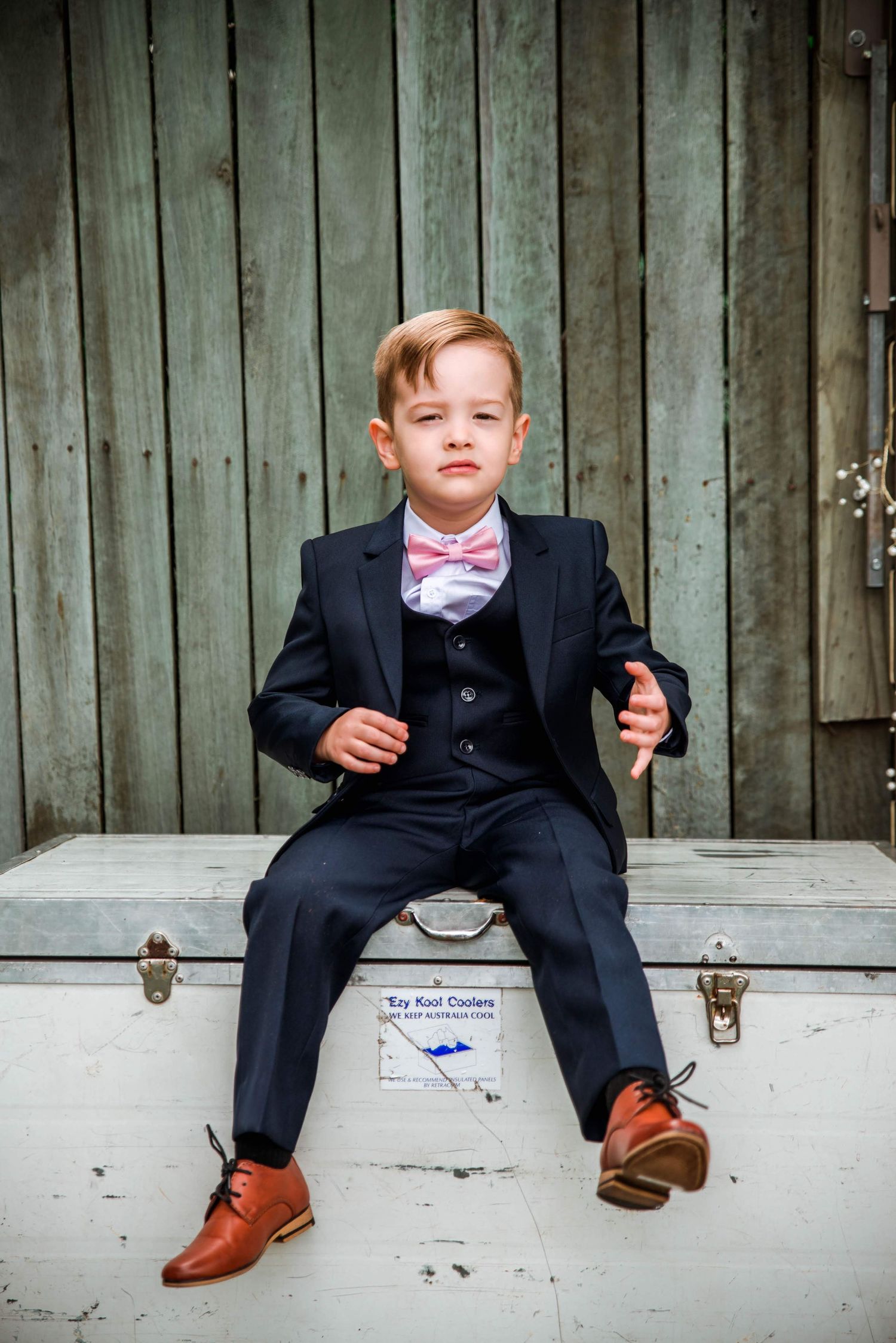 A young attendee in a formal navy suit and pink bowtie sits on a white chest.