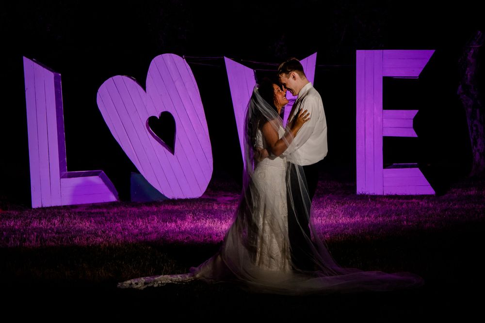 Dramatic nighttime portrait in front of illuminated purple LOVE letters.